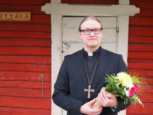 Pastori Pekka Hyppönen hymyilee ja hänellä on kädessään kukkakimppu.